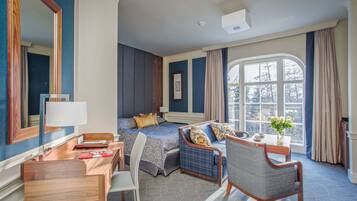 A hotel room with a bed, a desk, a chair, a window with curtains, and a view of trees.
