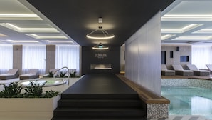 A modern hotel lobby with a pool area, featuring a reception desk, seating areas, and a staircase leading to the pool.