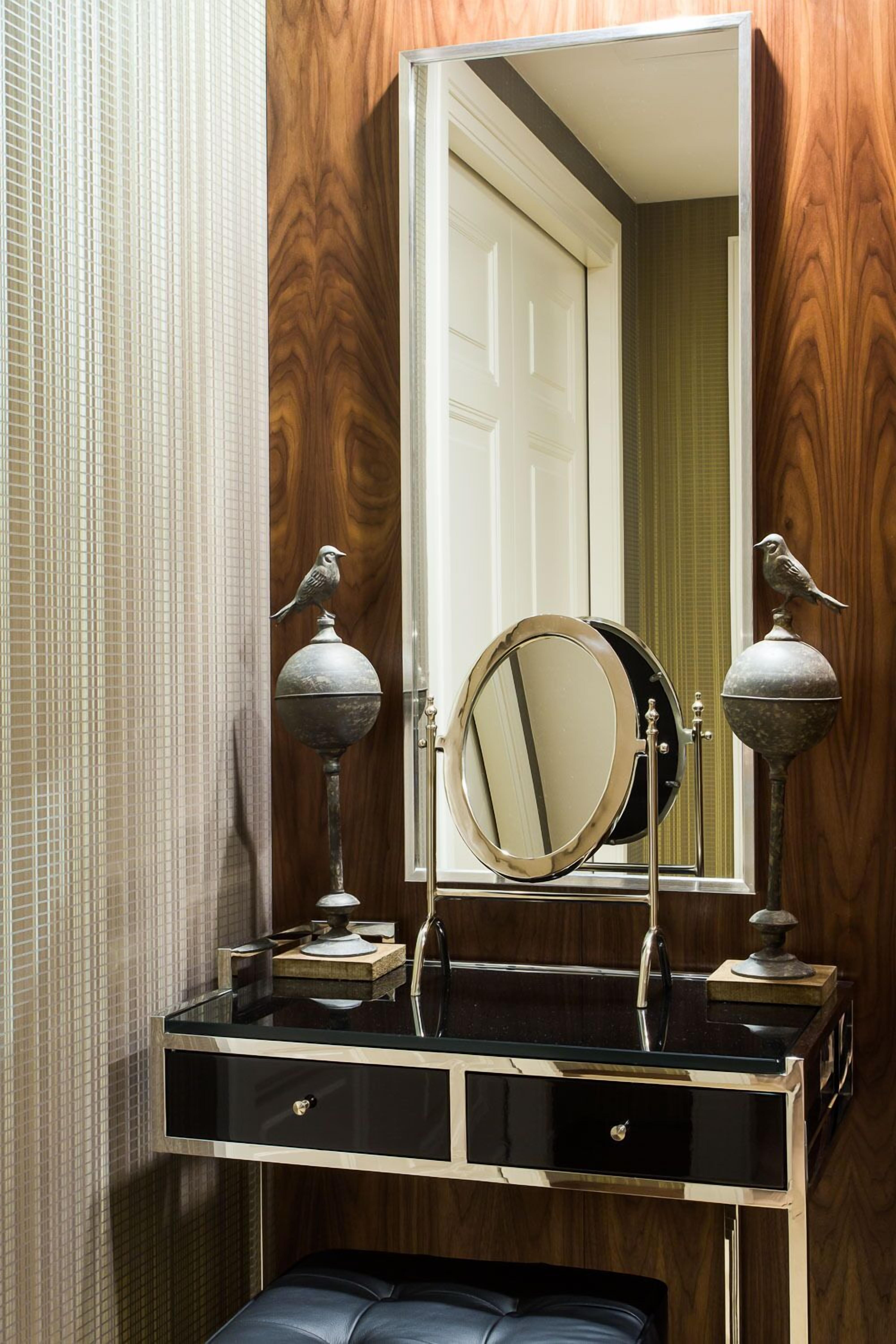 A bathroom vanity with a round mirror, two wall-mounted lamps, and a black leather bench.