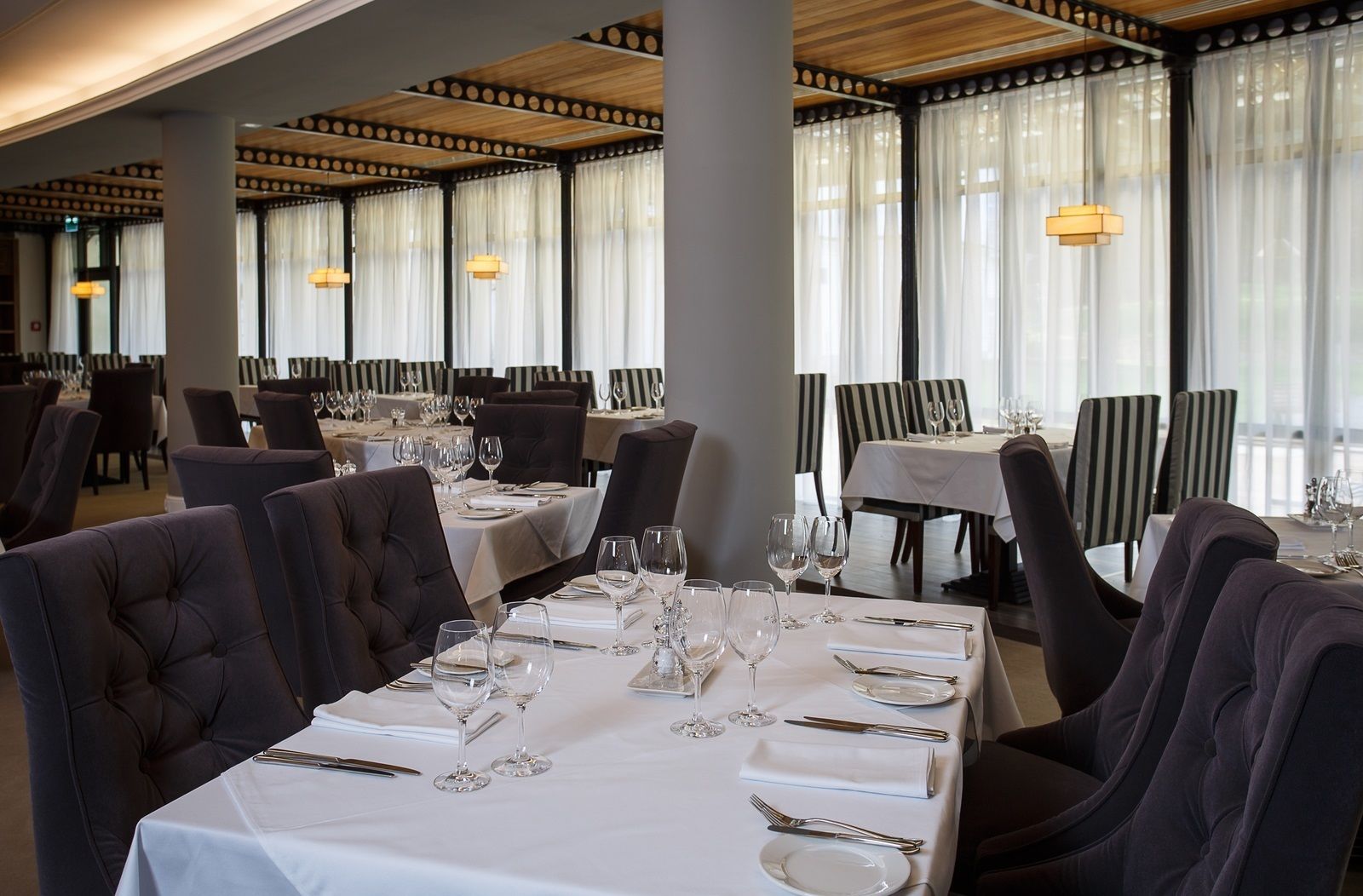 Un restaurant où les tables sont dressées pour le service, avec des chaises à rayures et un design moderne au niveau du plafond.