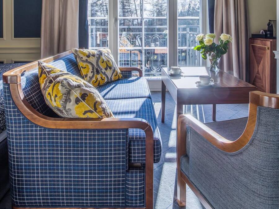 A cozy room with a large window, a sofa, a chair, and a small table with a vase of flowers.