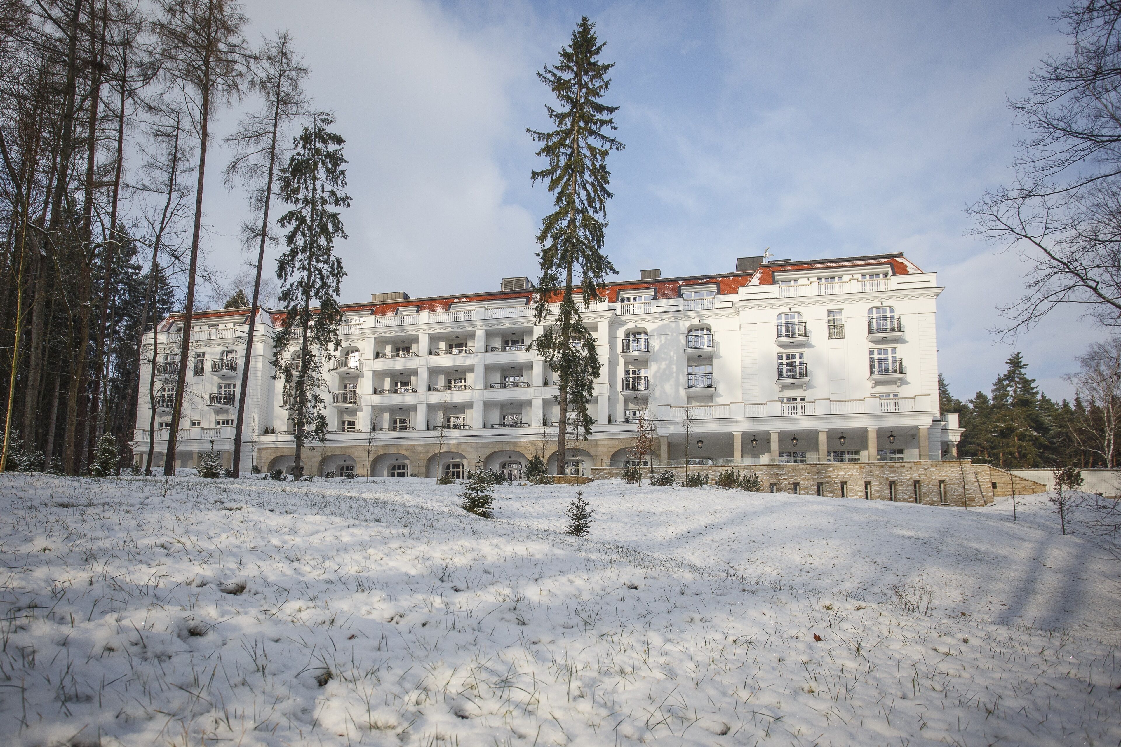 A large, multi-story building with a symmetrical facade, surrounded by snow-covered ground and tall evergreen trees.