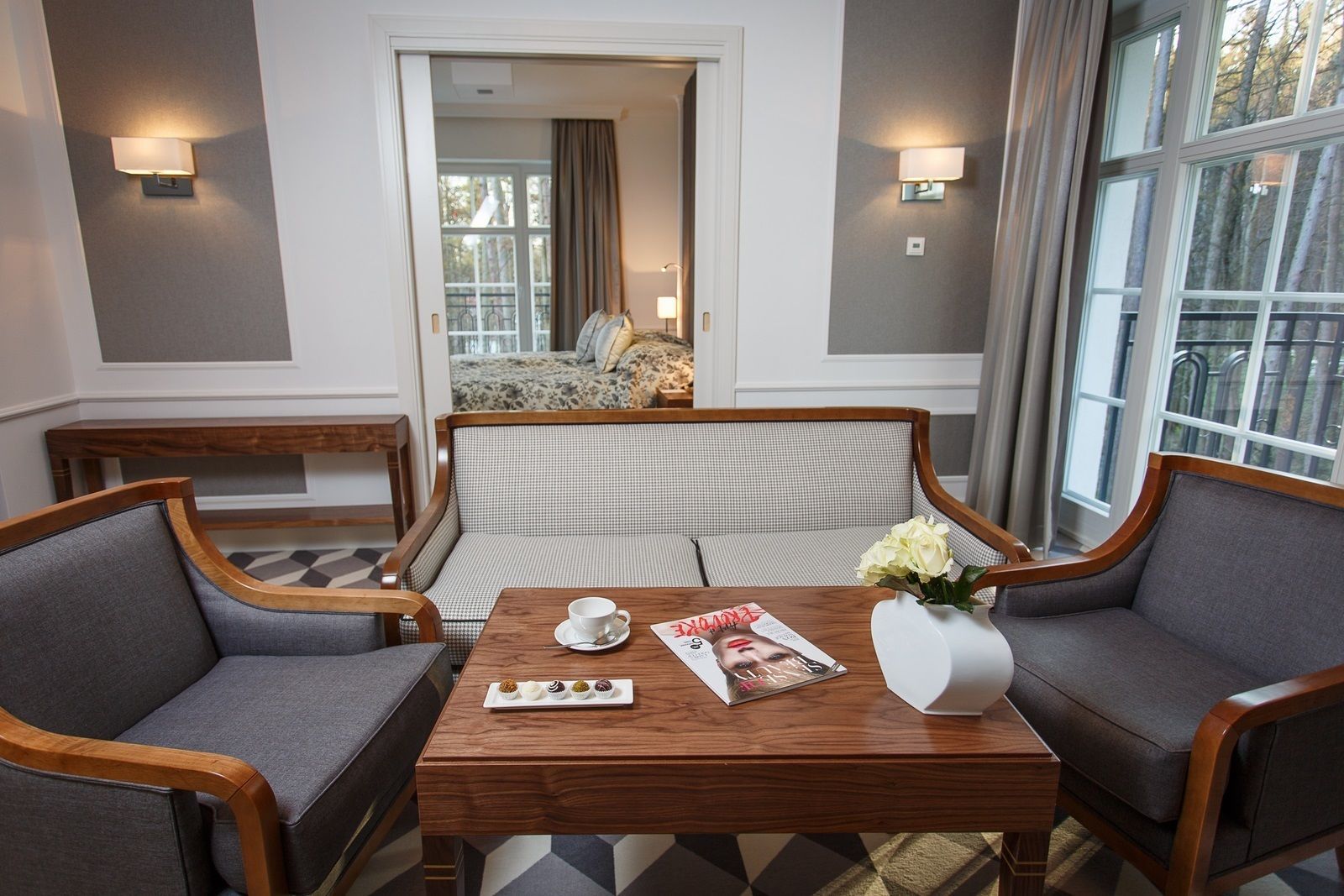 A hotel room with a sofa, two armchairs, a wooden coffee table, a magazine, and a vase with flowers.