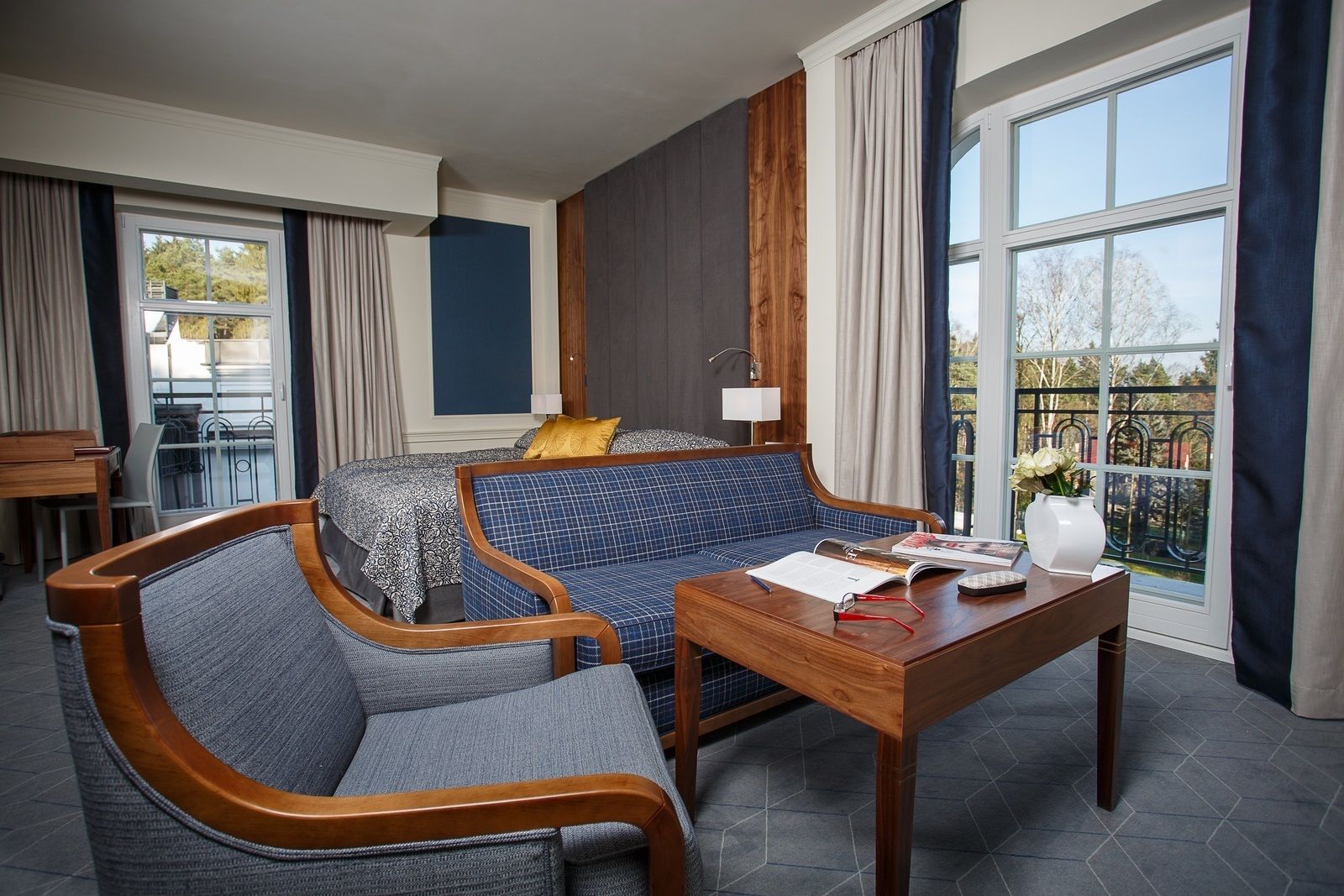 A modern hotel room with a sofa, armchair, and a small table with a book and glasses.