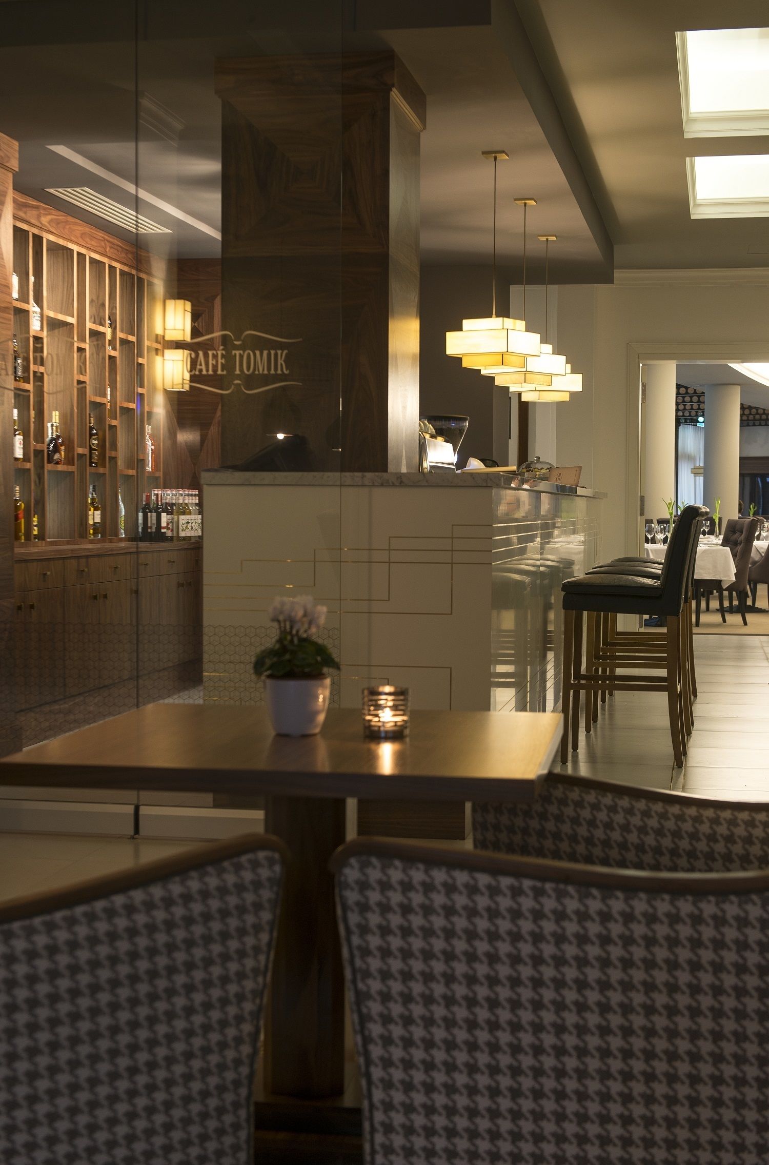A restaurant with a bar area, wooden cabinets, and a modern chandelier.