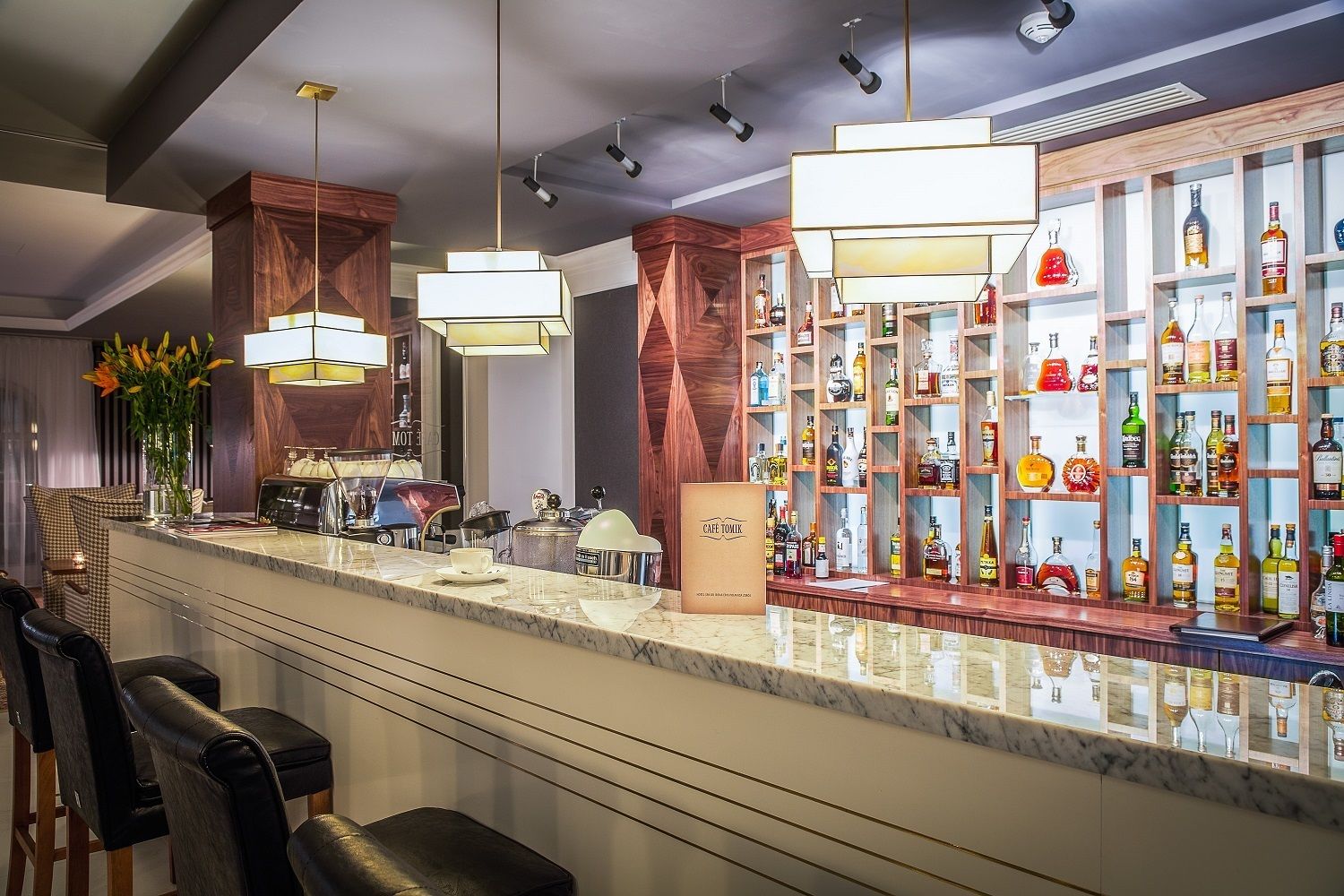 Un espace bar doté d’un comptoir en marbre, de plusieurs tabourets, d’une machine à café et d’une étagère bien garnie de bouteilles d’alcool.