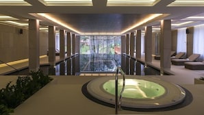A modern spa area with a hot tub, large windows, and a view of a forest.
