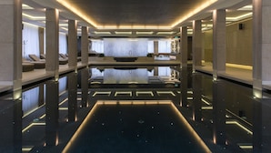 A modern hotel lobby with a central pool, seating areas, and a reception desk.