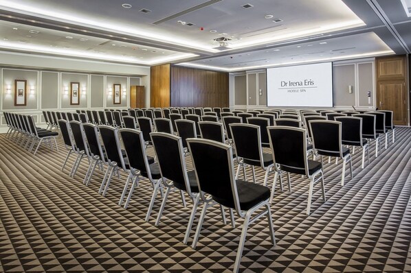 A conference room with rows of black chairs, a projector screen, and a patterned carpet.