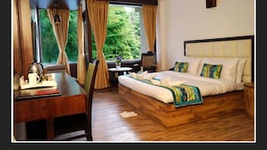 A hotel room with a wooden bed, a desk with a kettle, and a view of greenery through the window. - Whispering Inn by Vivaan (Manali)