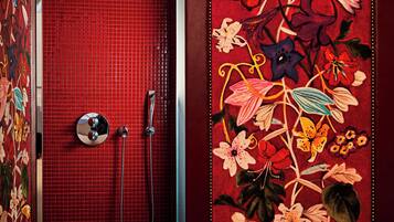 A bathroom with a red tiled wall, a shower with a chrome faucet, and a floral tapestry on the wall.
