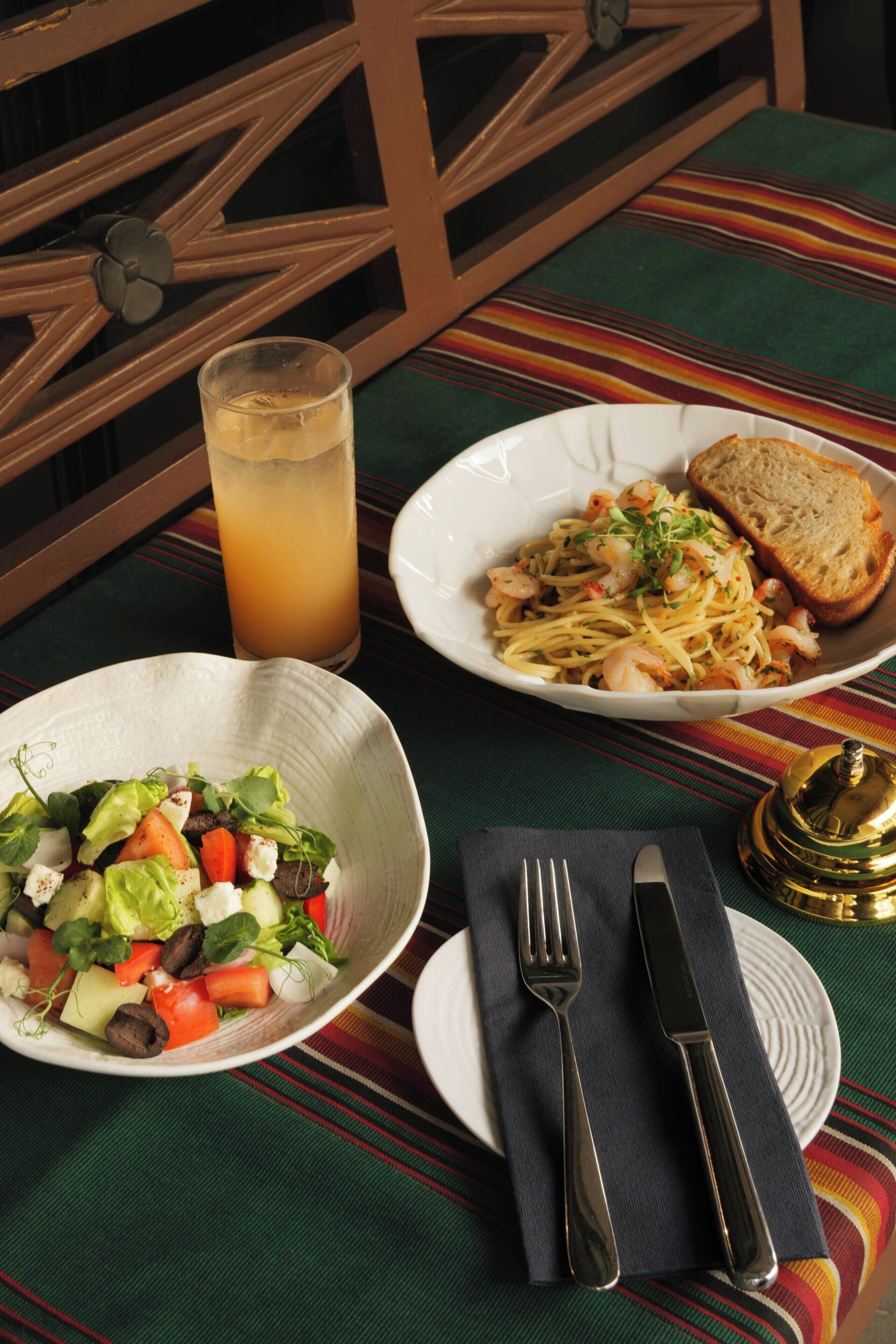 A table with a plate of pasta, a glass of juice, and a bowl of salad.