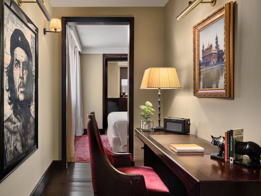 Un couloir d’hôtel avec un lit, un bureau doté d’une lampe, un tableau encadré et une statue.