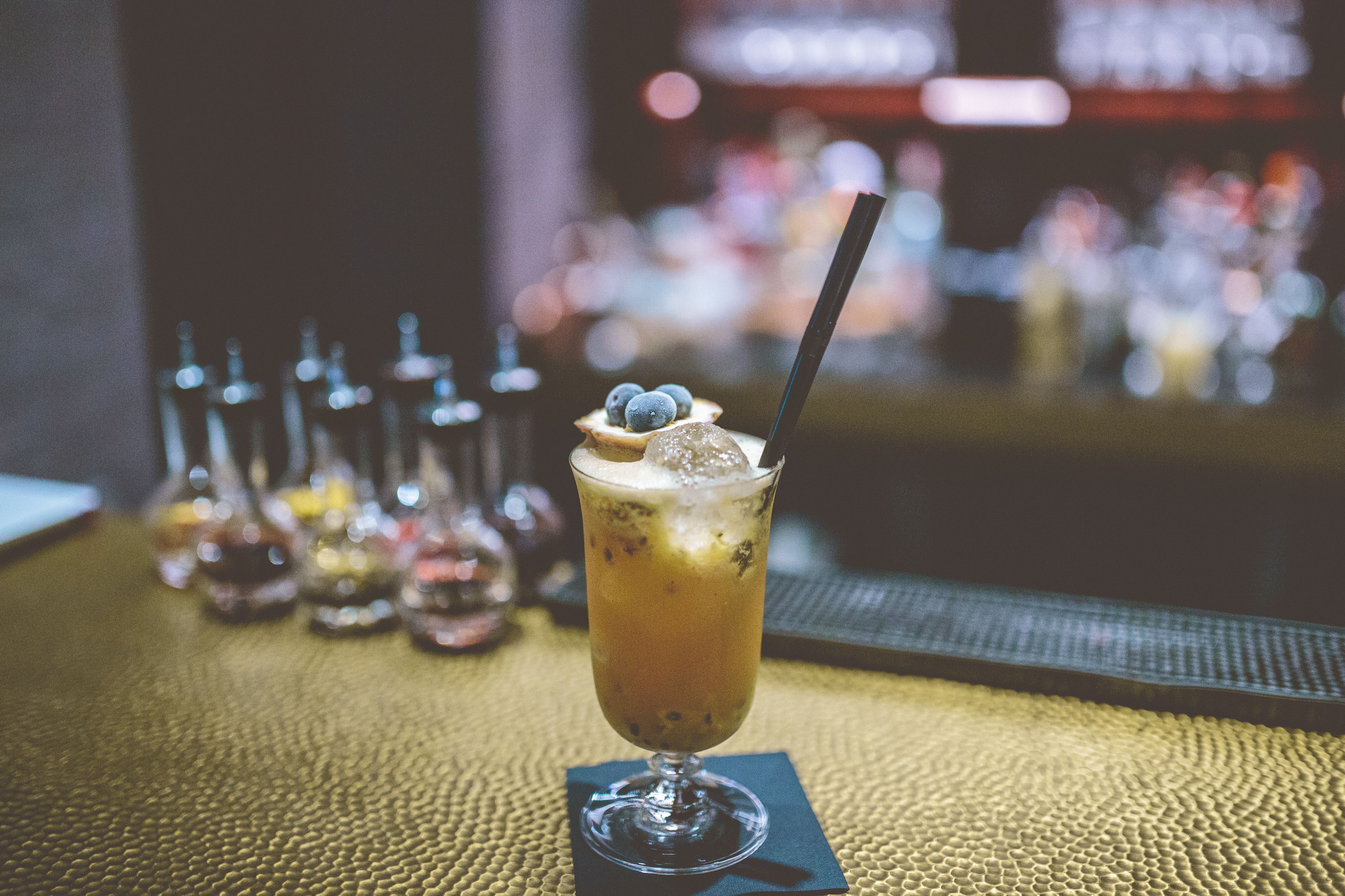 A cocktail with ice cubes and a straw in a glass, placed on a textured tablecloth.