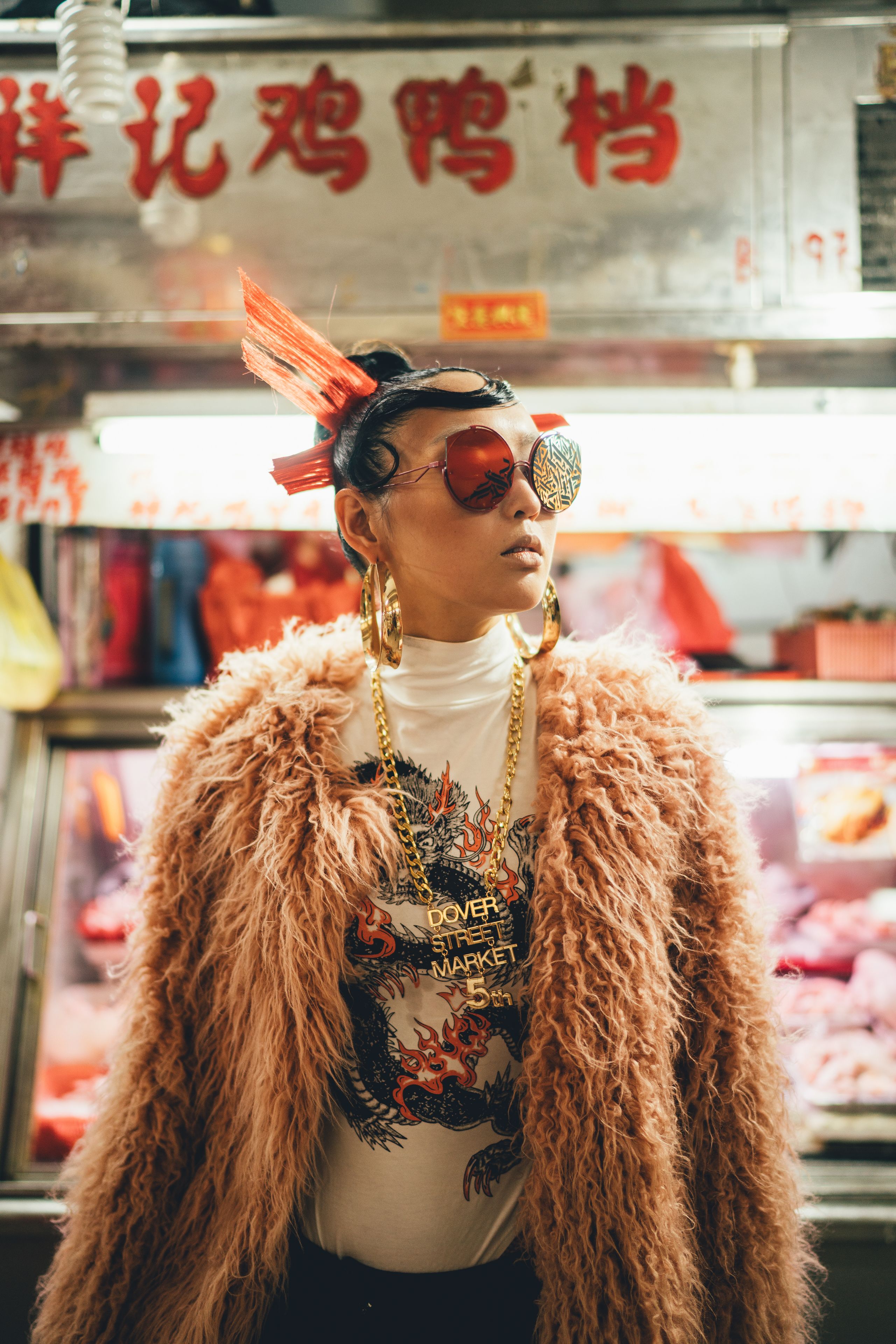 A person in a fur coat and sunglasses at a food market stall.