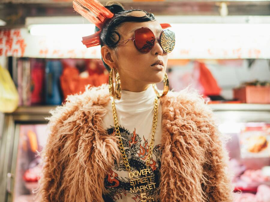 A person in a fur coat and sunglasses at a food market stall.