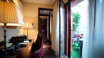 A hotel room with a desk, chair, lamps, and a view of the outdoor patio.