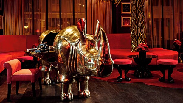 A luxurious room with a large, shiny metallic rhinoceros sculpture, red sofas, and a modern interior design. - The Vagabond Club, Singapore, a Tribute Portfolio Hotel (Singapore)
