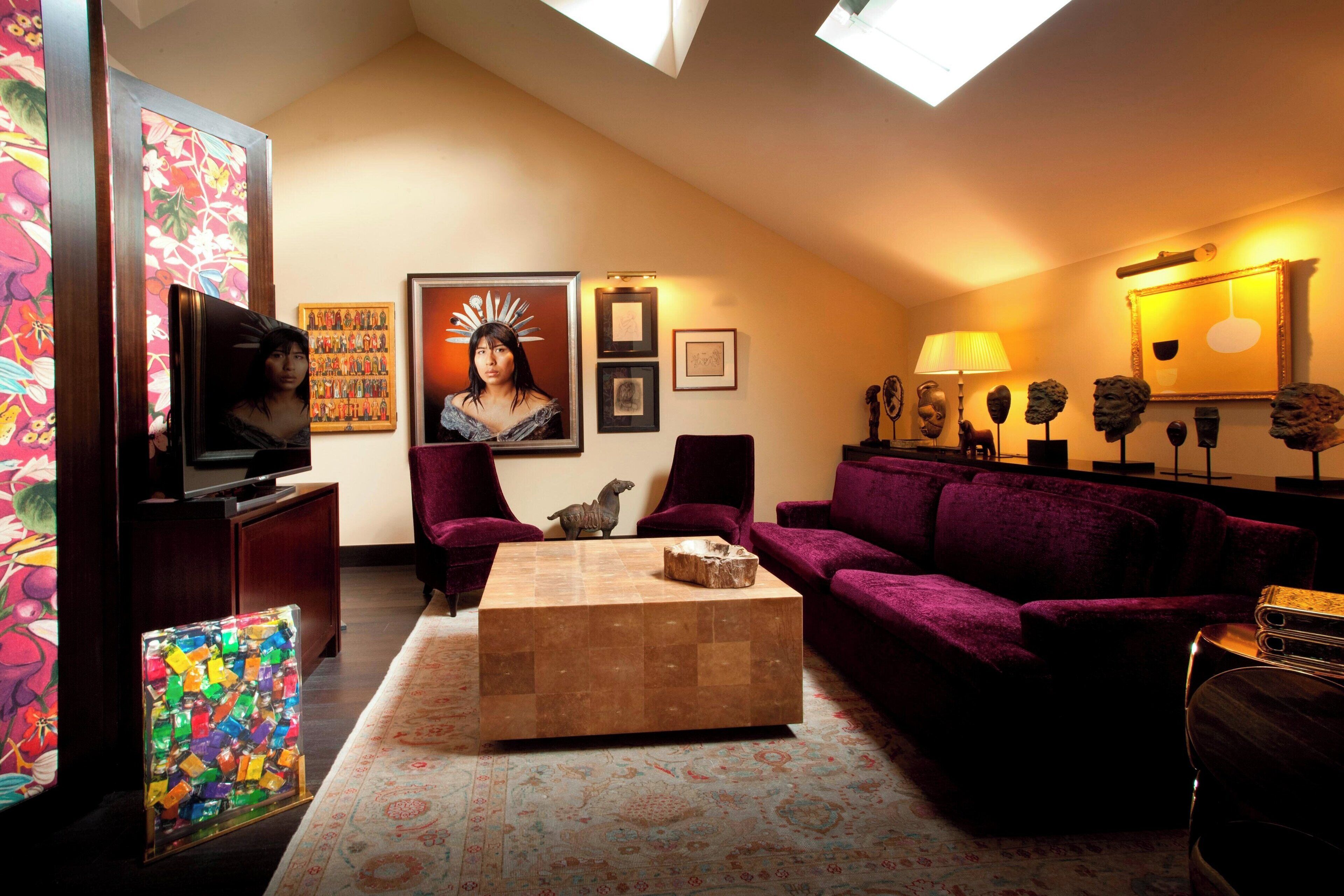 A living room with a high ceiling, a large window, a flat-screen TV, a coffee table, a purple sofa, and a patterned rug.
