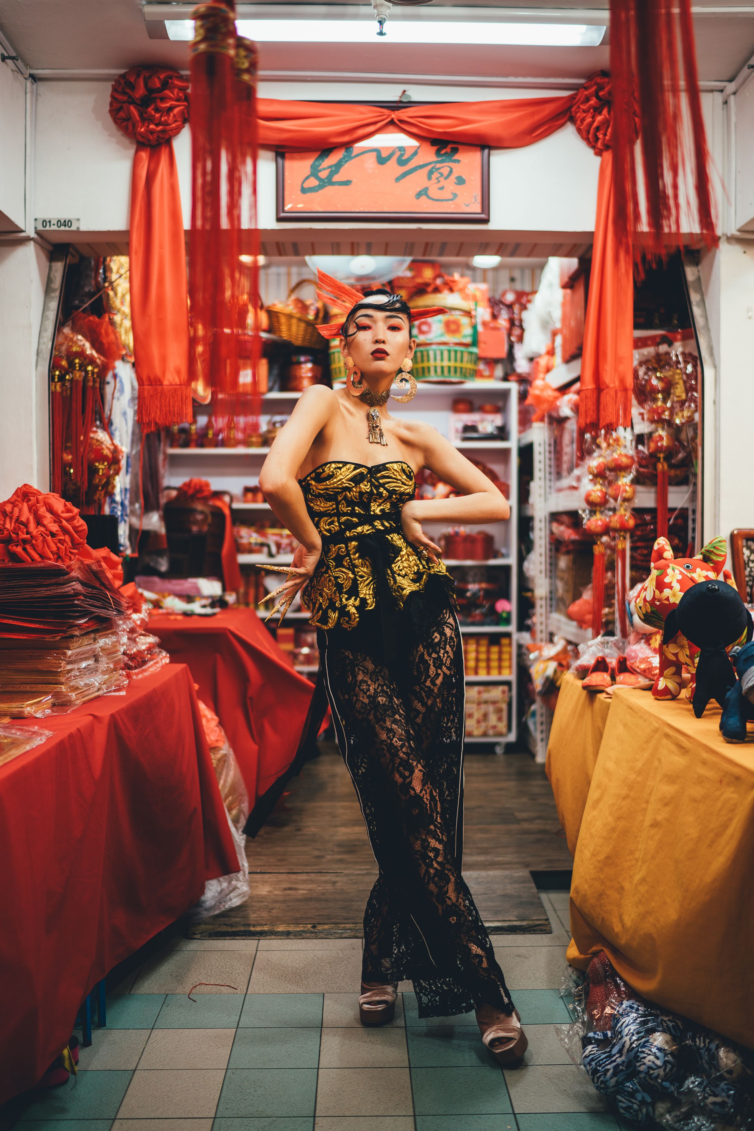Eine Frau in einem schwarzen Spitzenkleid steht in einem Geschäft mit roten Dekorationen und Regalen voller Waren.