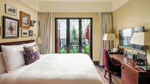 A hotel room with a bed, a desk with a computer, a TV, and a view of an outdoor patio with a table and chairs. - The Vagabond Club, Singapore, a Tribute Portfolio Hotel (Singapore)