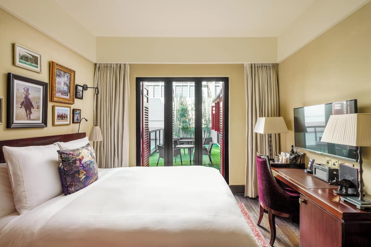 A hotel room with a bed, a desk with a computer, a TV, and a view of an outdoor patio with a table and chairs.