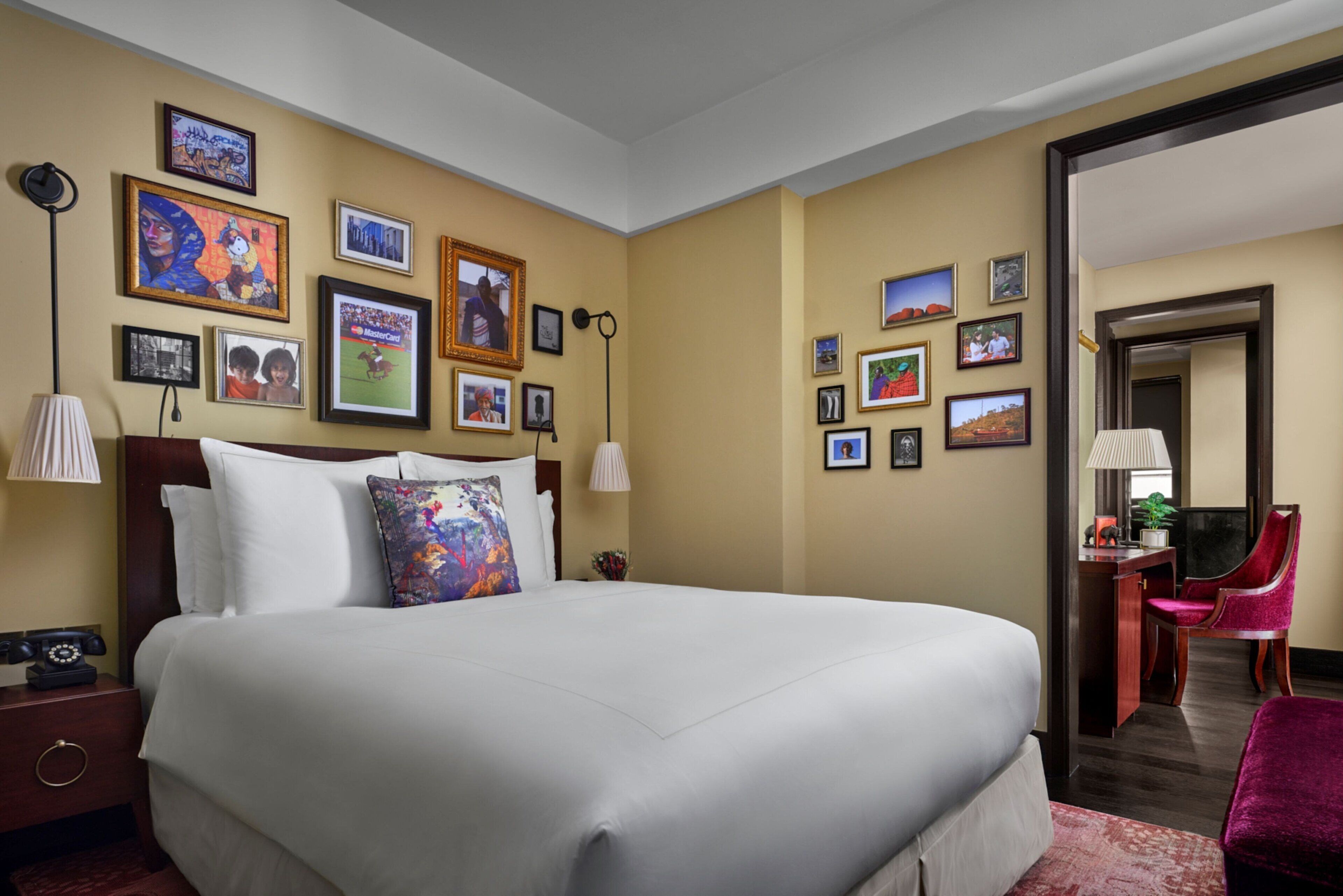 A hotel room with a large bed, a desk with a chair, and various framed pictures on the walls.