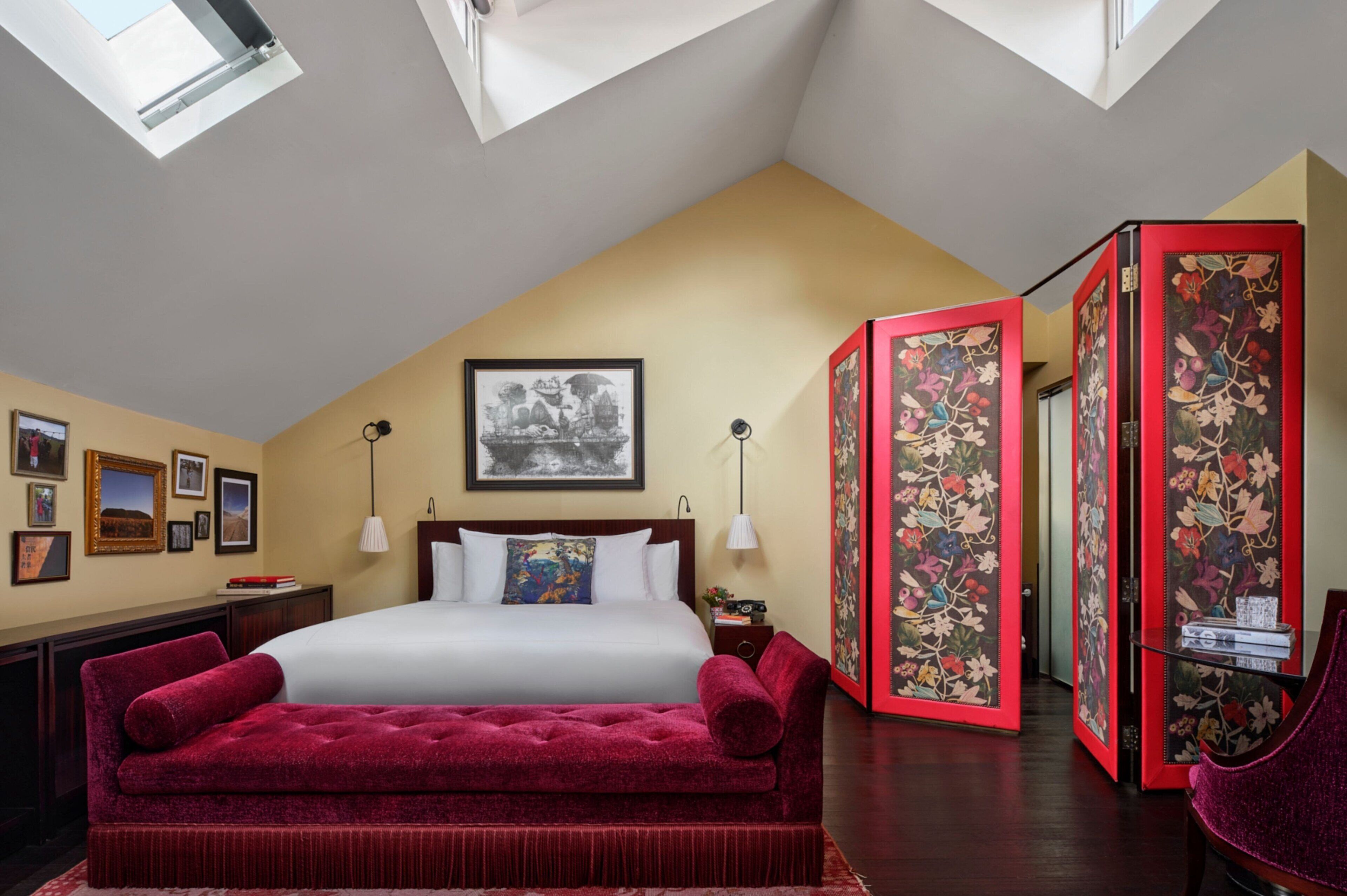 A hotel room with a large bed, a red sofa, a desk, a lamp, and a wall with framed pictures.