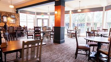 A restaurant interior with multiple dining tables and chairs, large windows, and a patterned wall.