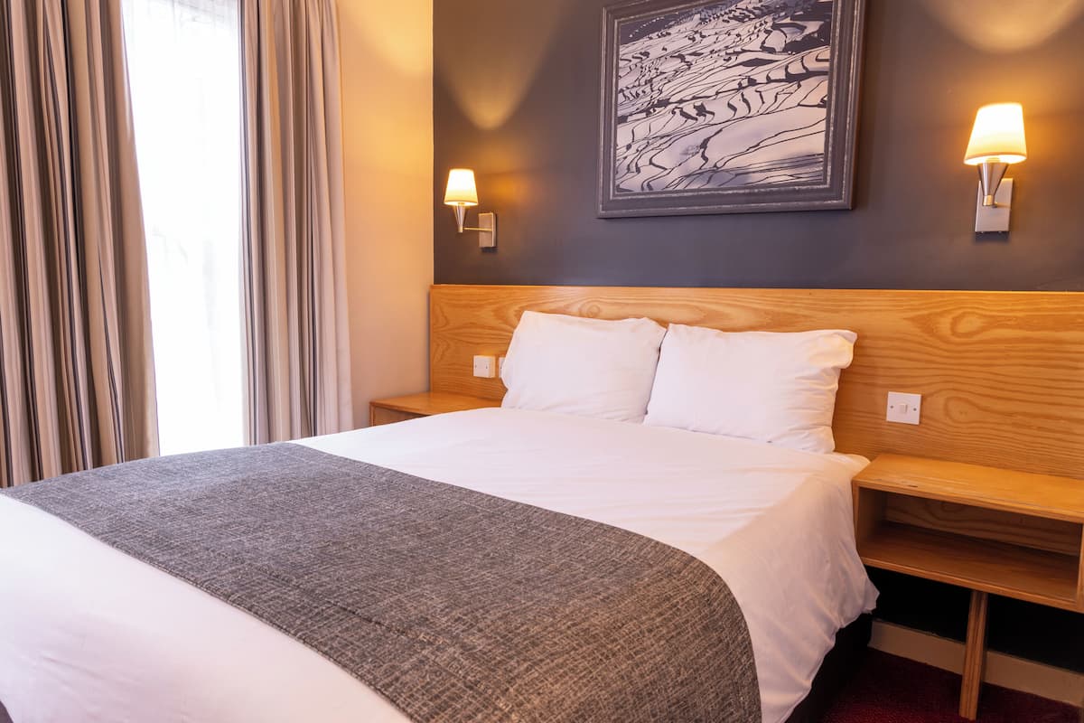 Habitación de hotel con una cama grande, dos mesitas de noche, una lámpara de pared y un cuadro enmarcado.