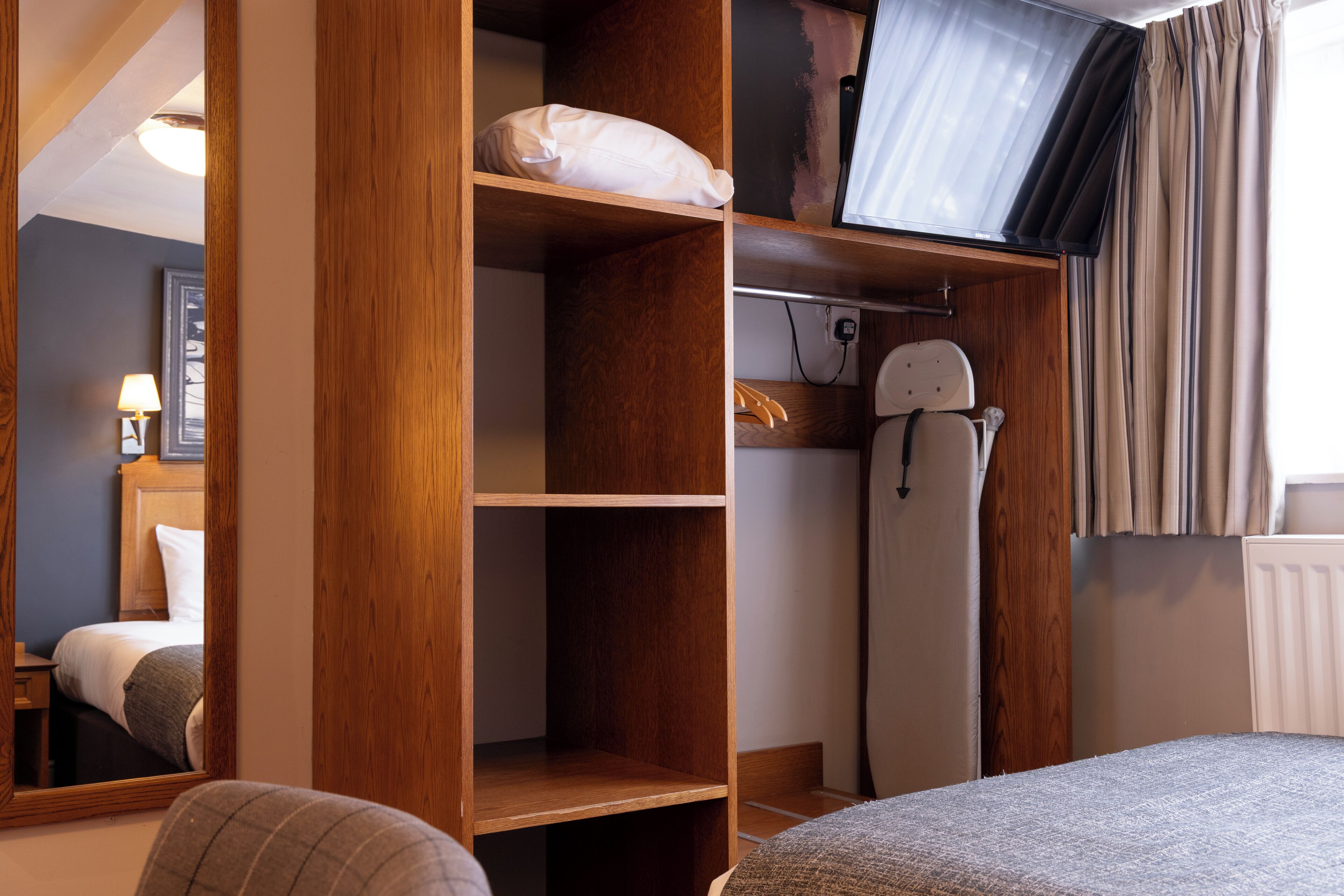 A bedroom with a wooden wardrobe, a bed, a mirror, a television, and a radiator.