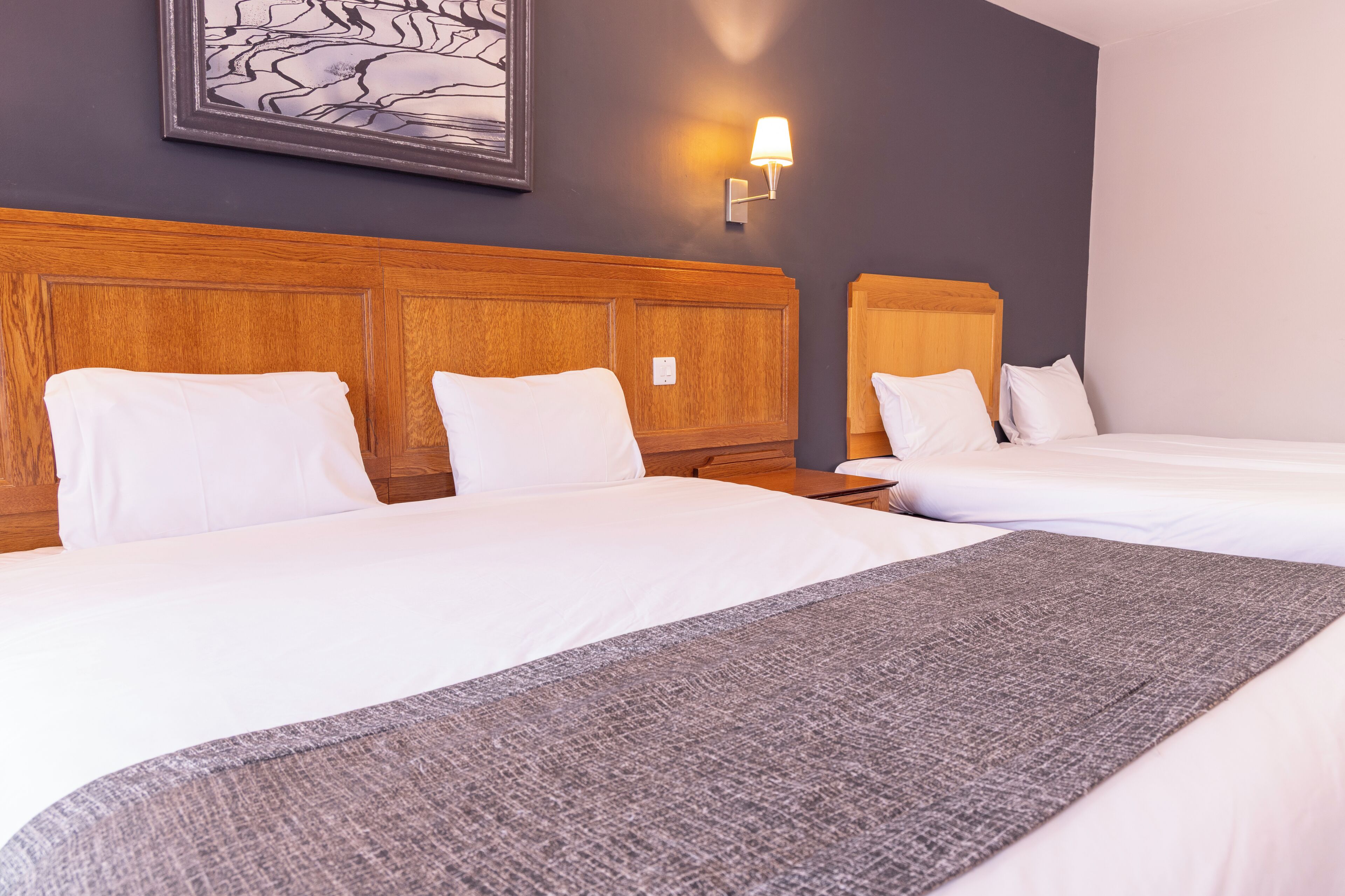 Ein Hotelzimmer mit zwei Betten, einem Holzkopfteil, einer Wandlampe und einem gerahmten Kunstwerk.