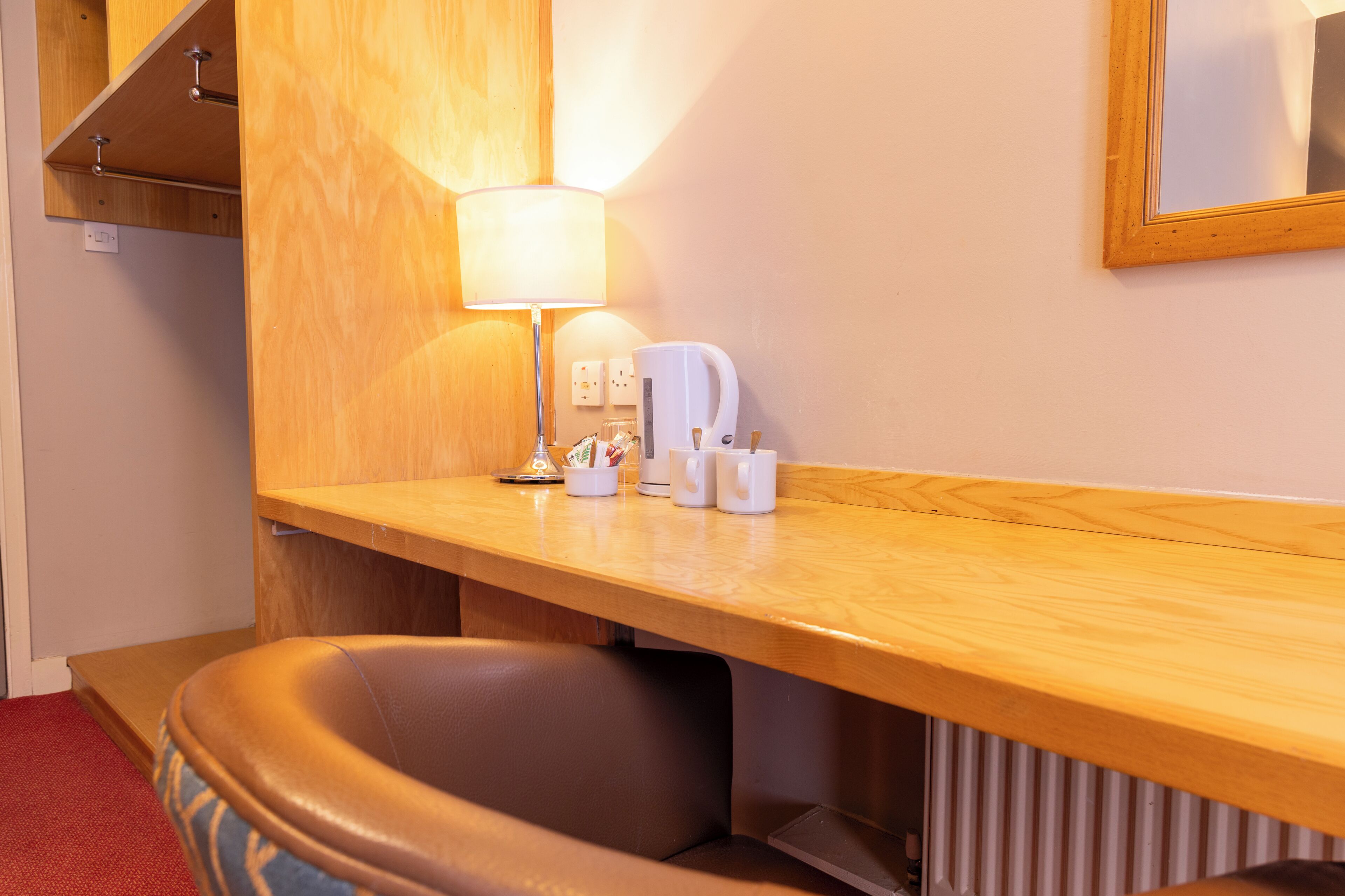 Een hotelkamer met een houten bureau, een lamp, een koffiezetapparaat en een stoel.
