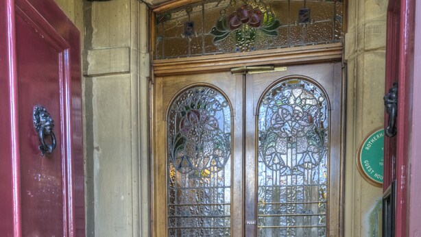 A wooden hotel entrance with a double door, a doormat, and a tiled floor.