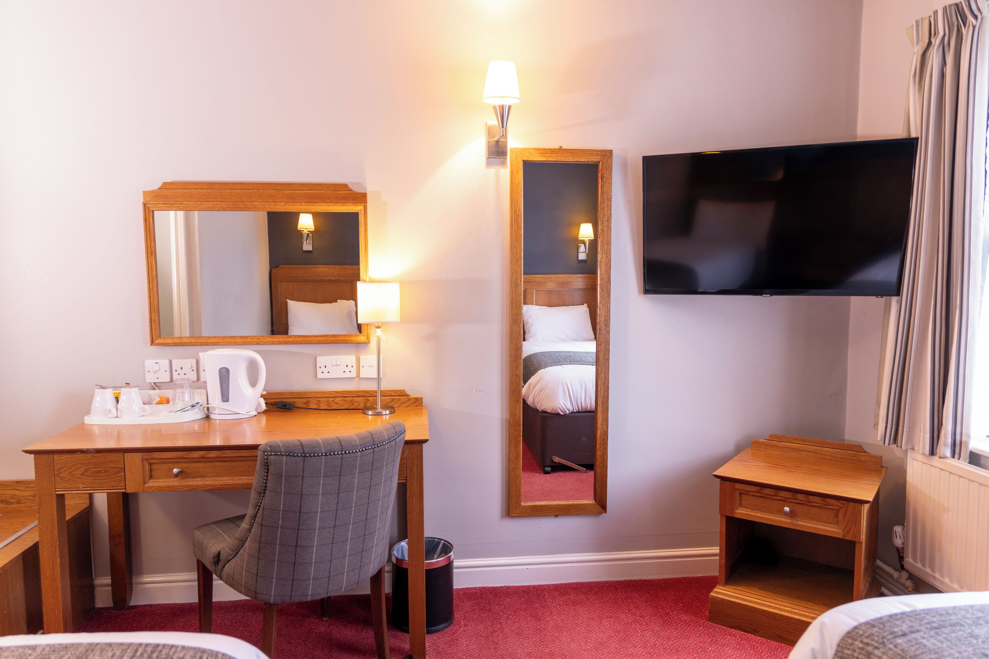 Une chambre d’hôtel avec un bureau en bois, une chaise, un lit, une télévision, un miroir et une petite table de chevet.