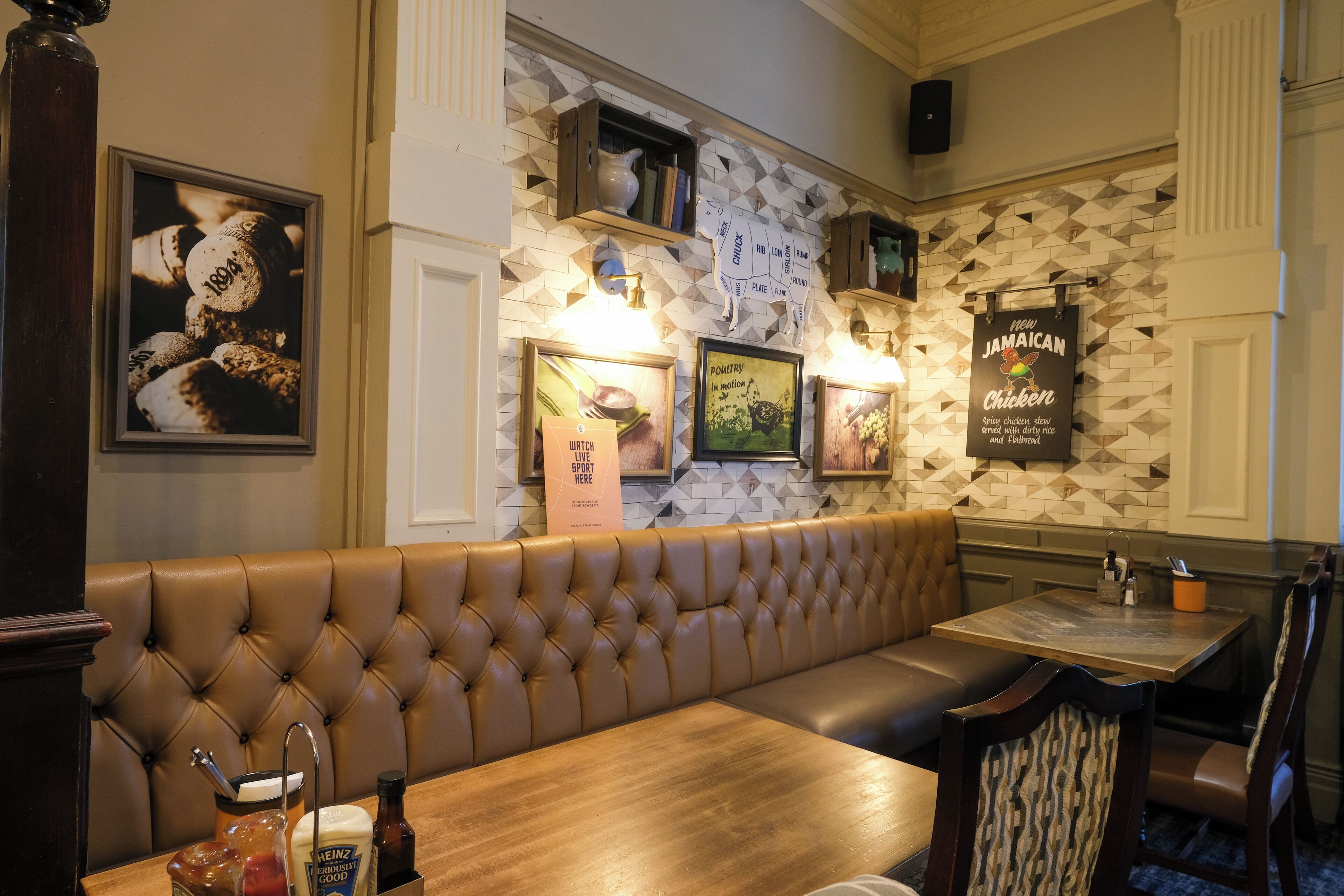 A restaurant interior with a brown leather booth, wooden tables, and framed pictures on the wall.