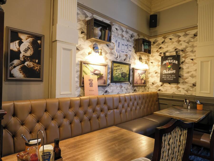 A restaurant interior with a brown leather booth, wooden tables, and framed pictures on the wall.