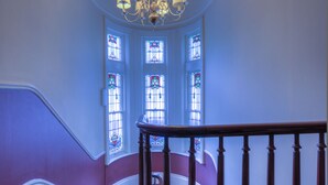 A grand staircase with a patterned carpet, a chandelier, and stained glass windows.