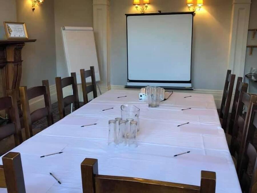 Ein Konferenzraum mit langem Tisch, Stühlen, einer Projektionsleinwand und Wandlampen.