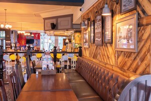 Interior de restaurante com paredes de madeira, área de bar e seção de assentos com encosto alto.