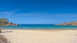 Una playa con aguas azules cristalinas, arena y afloramientos rocosos.