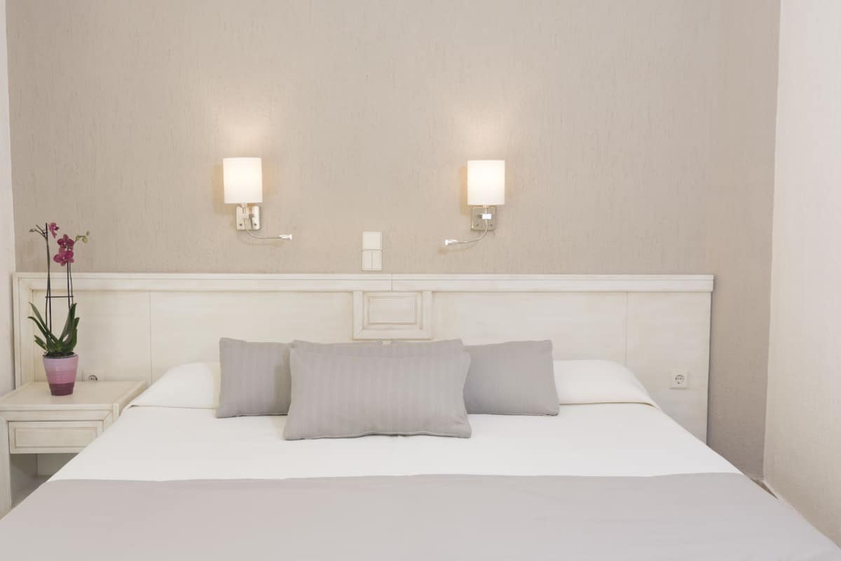 Habitación de hotel con una cama grande, dos lámparas de noche, una mesita de noche con una planta en maceta y un aplique de pared.