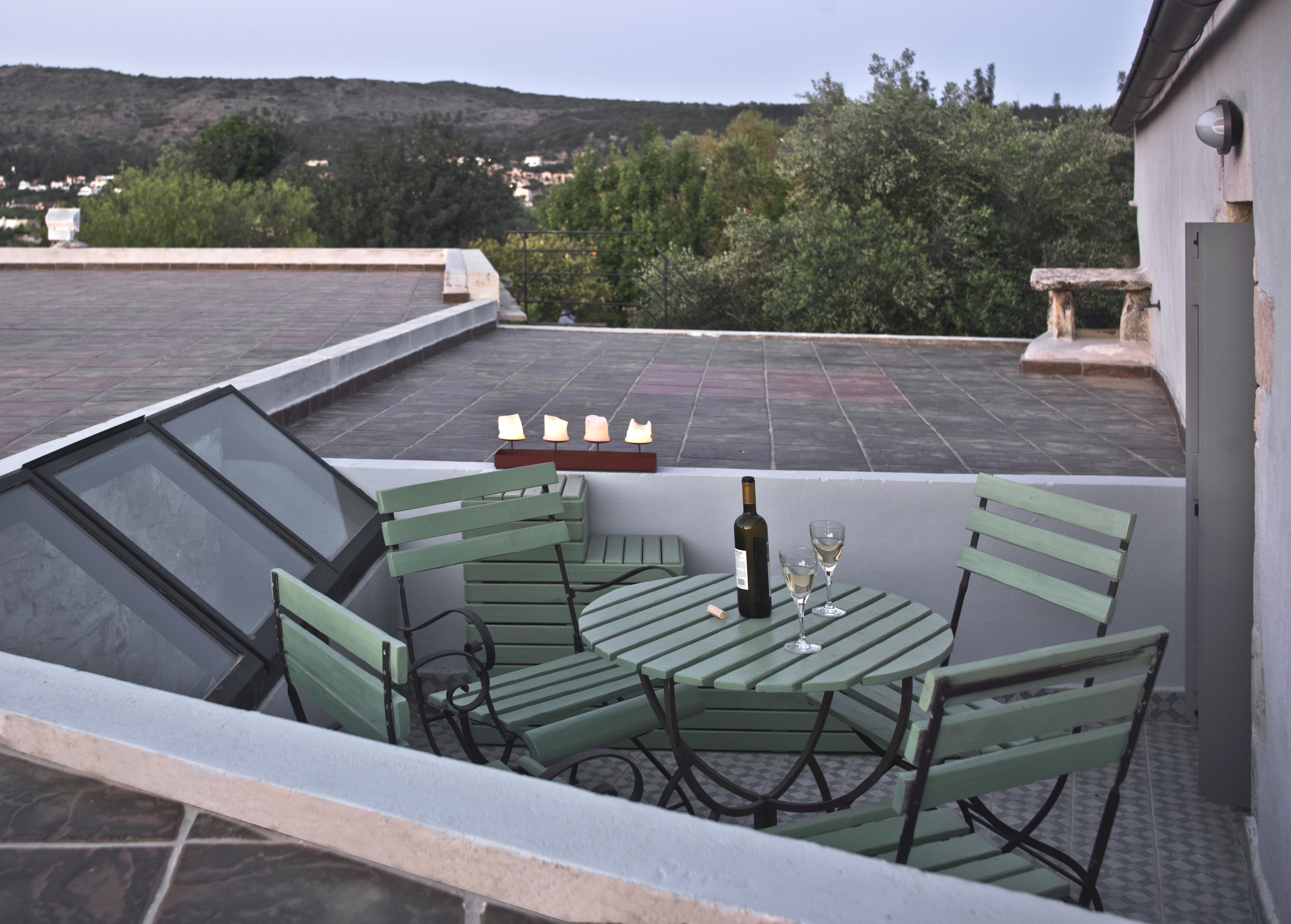 A rooftop terrace with a table and chairs, a bottle of wine, and candles.