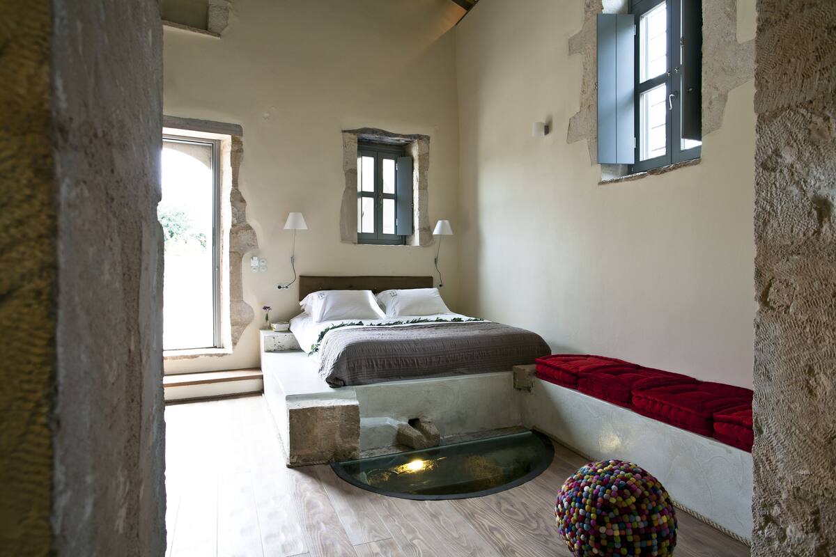 A bedroom with a bed, a small window, a red bench, and a decorative ball.