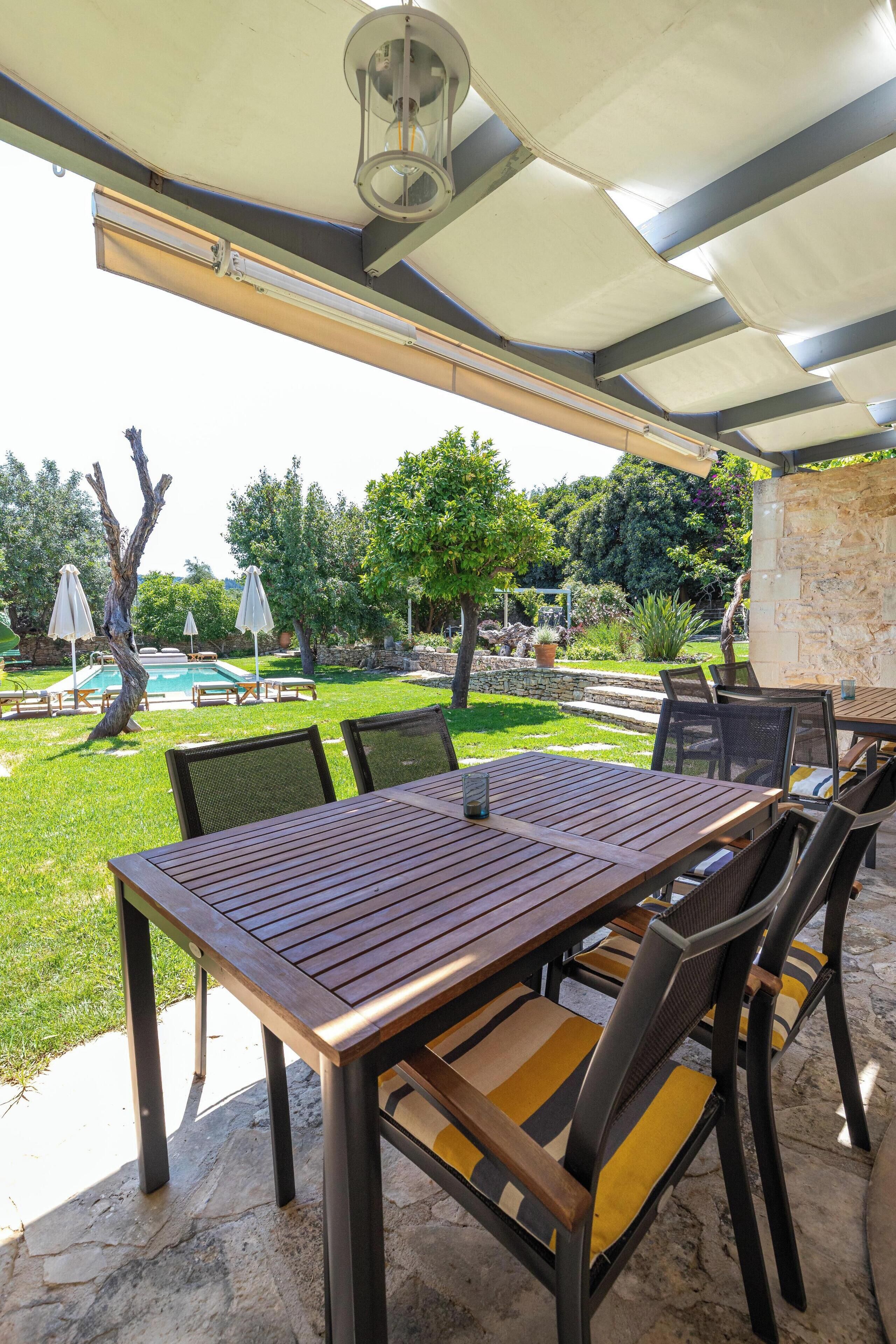 Un patio al aire libre con una mesa, sillas, una piscina y un muro de piedra.