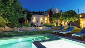 Un edificio de piedra con piscina y sillones de descanso al frente.