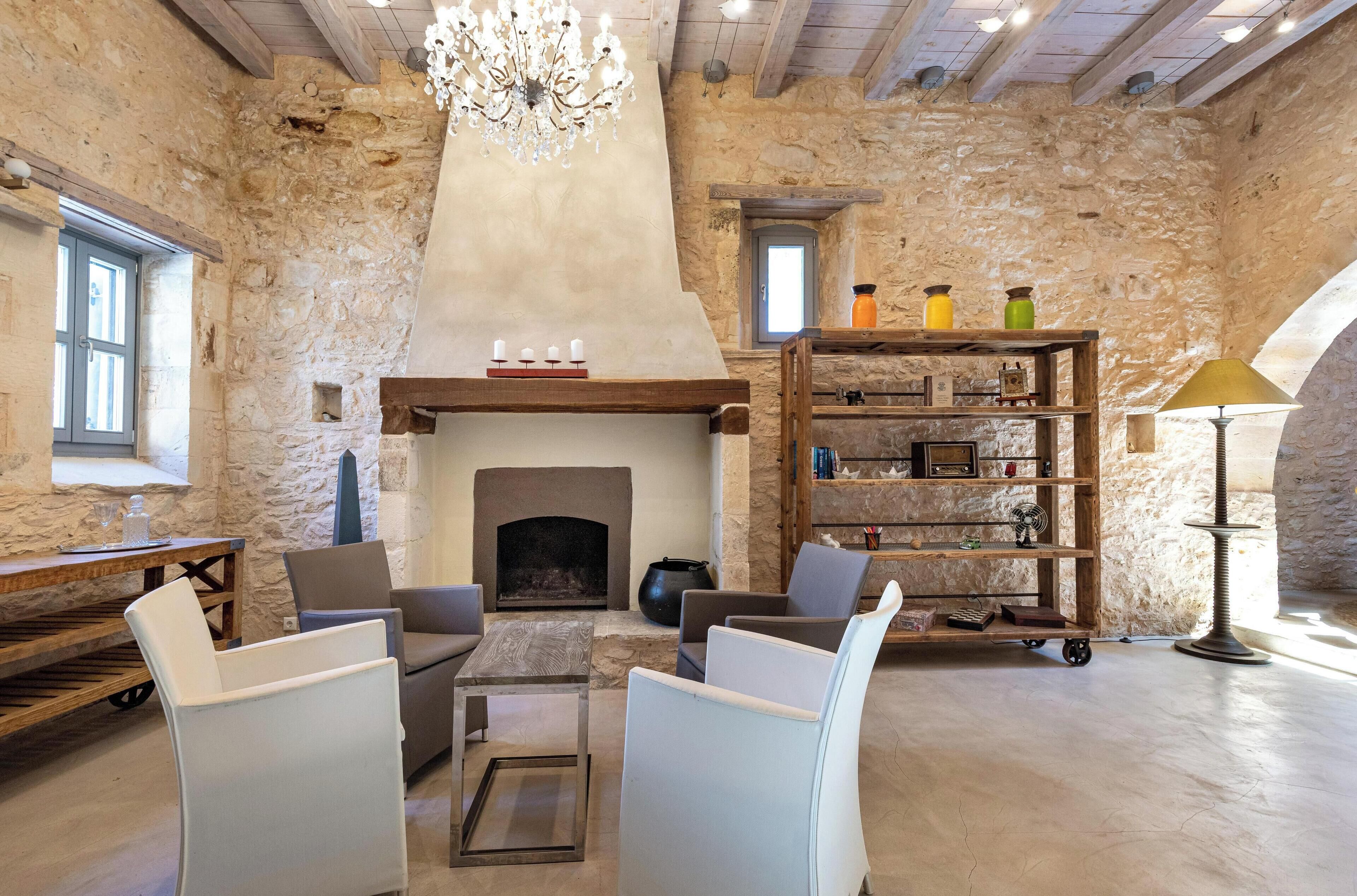 A rustic stone interior with a fireplace, seating area, and a wooden bookshelf.