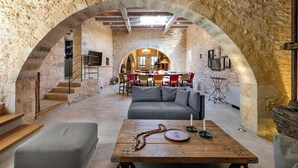Interior rústico de piedra con una zona de comedor central, un sofá y una mesa de madera con velas.