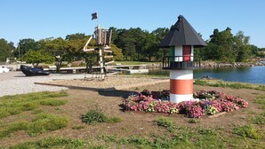 A lighthouse with a flag, surrounded by flowers, near a body of water. - Segelfartyget Libelle (Oxelosund)