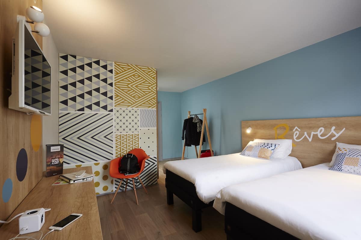 Ein Hotelzimmer mit zwei Betten, einem Schreibtisch mit einem Laptop, einem Stuhl und einem Kleiderschrank.